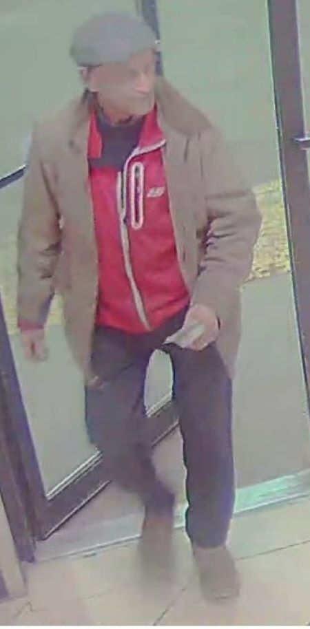 Un homme d&rsquo;un certain &acirc;ge portant une casquette b&eacute;ret, un manteau beige et, en dessous, une veste rouge &agrave; fermeture &eacute;clair. 