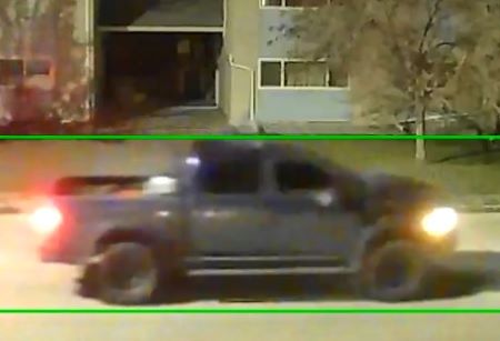 An image of a dark truck driving at night in a residential area. 