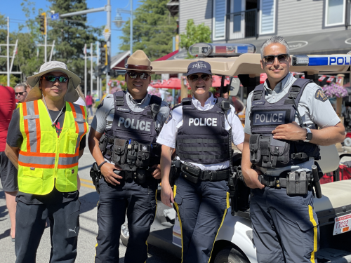 volunteer in a safety vest standing next to three RCMP officers at a community event and everyone is smiling