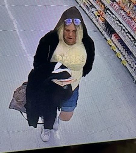 An image of a suspect in a black hooded jacket with a yellow shirt underneath, and blue jean shorts. She has sunglasses on top of her head. 