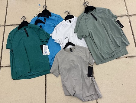 Seize t-shirts, avec leurs cintres, &agrave; plat sur un plancher carrel&eacute;.