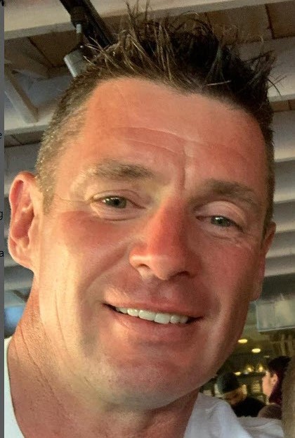 Photo prise de la t&ecirc;te aux &eacute;paules de Stan Cappis qui sourit et qui porte un tee-shirt blanc.