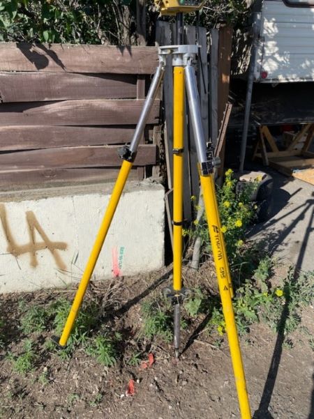 A yellow tripod near a fence. 