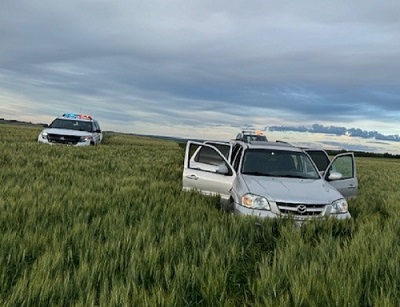 Suspect vehicle stopped in a field by two police vehicles with emergency lights on