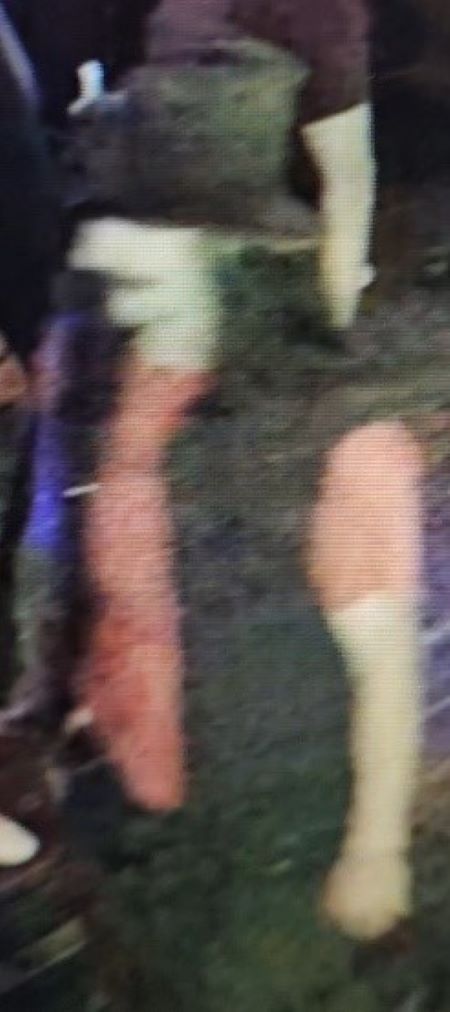 A blurry image of a man with a hat on, orange shirt, and black vest. 