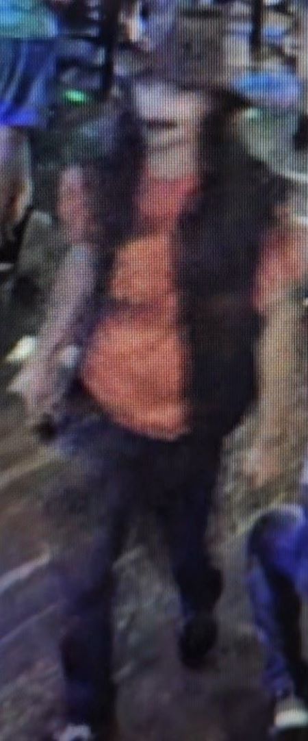 A blurry image of a man with a hat on, orange shirt, and black vest. 