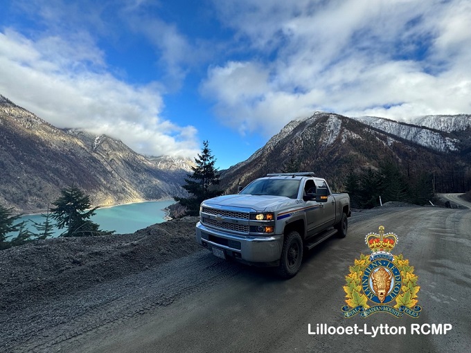 Pictured is an RCMP vehicle on a gravel road West of Lillooet with a blue lake in the back. 