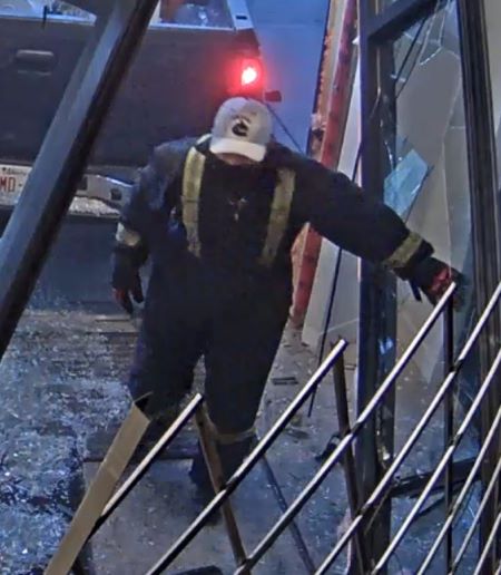 Un suspect portant une combinaison bleue avec des bandes jaunes &agrave; haute visibilit&eacute;, un masque, des gants et une casquette de couleur claire avec un logo fonc&eacute;.