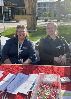Photo of two Victim Services staff members sitting at an information booth at a community event. 
