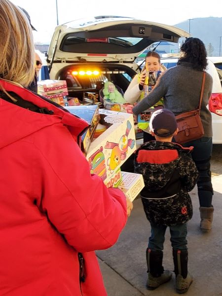 : People hand toys and packages to a police volunteer, who is stuffing them into a police cruiser.