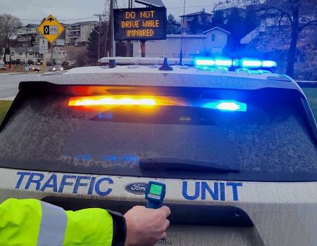 A traffic unit police vehicle with its lights on is parked in front of digital sign with &lsquo;Do not drive while impaired&rsquo; text displayed. A police officer&rsquo;s arm was stretched across the back end of the vehicle. A roadside breath test is in the officer&rsquo;s hand. 