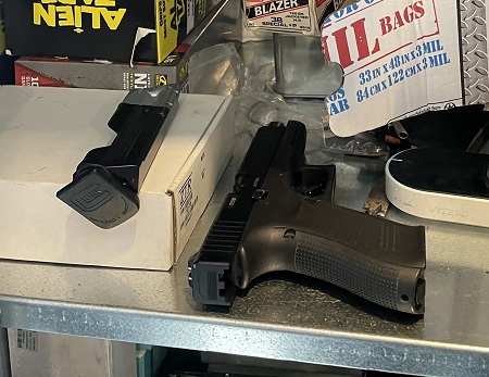 A shelf with a black handgun, a magazine and several boxes of miscellaneous items