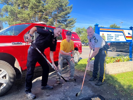 Fire chief and police supervisor pose with hockey sticks