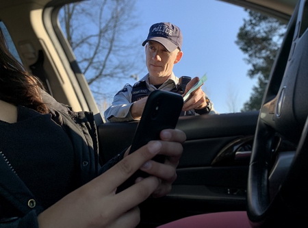 Richmond RCMP officer standing at window of car looking at driver holding electronic device