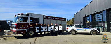 Photo of police officers, firefighters and community members holding a sign that says $60,000. They are standing in front of a fire truck and a police car. 