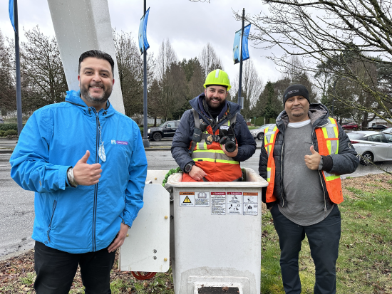 Deux hommes, le pouce lev&eacute;, se tiennent de part et d'autre d'un homme install&eacute; dans une nacelle &eacute;l&eacute;vatrice et muni d&rsquo;un appareil photo