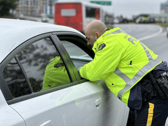Un policier portant un gilet r&eacute;flecteur se penche sur la vitre du c&ocirc;t&eacute; passager d&rsquo;un v&eacute;hicule