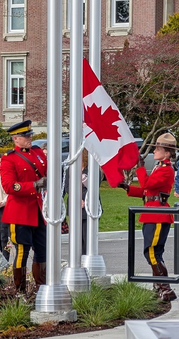 Two RCMP officers wearing Red Serge raising the Canadian flag at the flagpole
