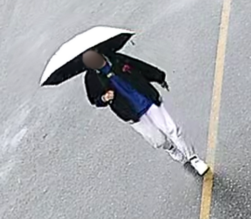 Photo of first witness Asian wearing a black jacket, blue shirt, white pants, white running shoes and carrying a white and black umbrella