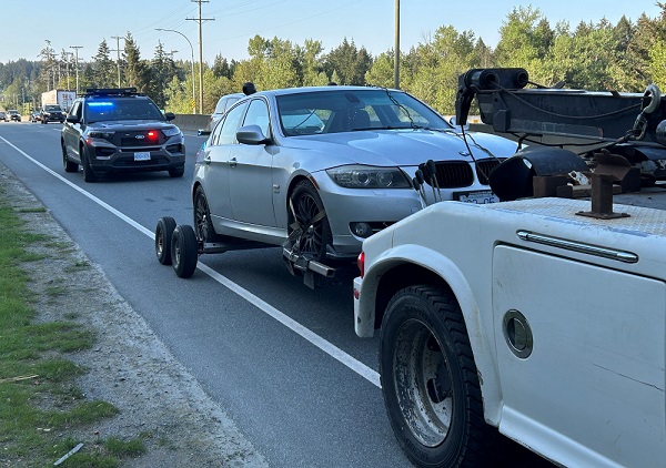 A BC Highway Patrol vehicle supervises as a grey BMW gets towed to an impound lot