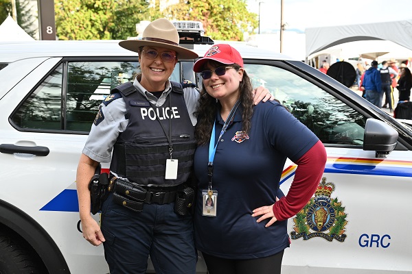 A Mountie in a Stetson standing next to an RCMP employee, both standing in front of an RCMP police vehicle
