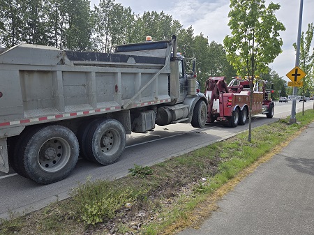 A large dump truck hooked up to a red tow truck on the side of the road.