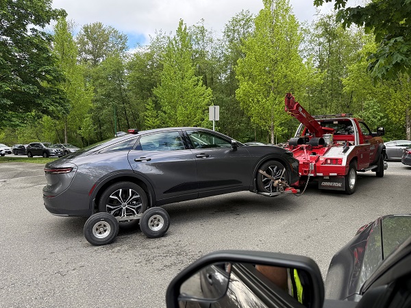 A grey 4 door sedan on the back of a red tow truck