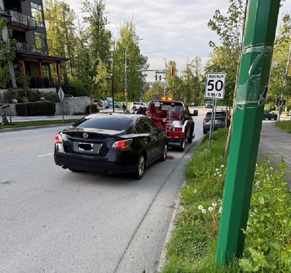 A black sedan on a residential street, next to a 50km/h speed sign, getting loaded onto a red tow truck