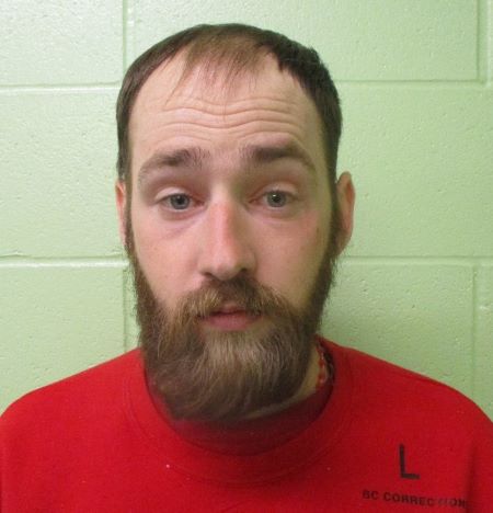 A current photo of Taylor Dueck in which he is wearing an orange shirt, has short hair, and a full beard.