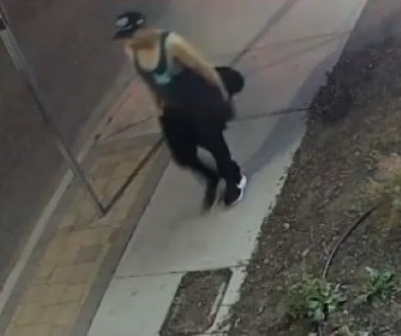 Un homme qui porte un chapeau, une camisole et un pantalon noirs marche sur le trottoir.