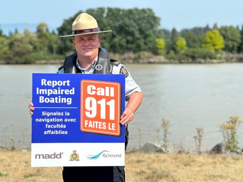 Richmond RCMP officer holding a sign that says report impaired boating.