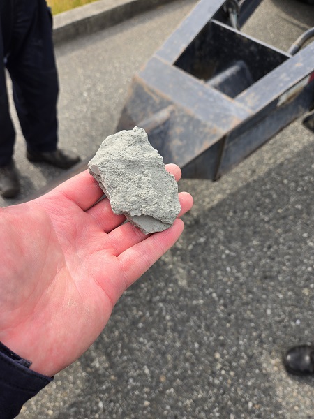 A rock in the hand of a commercial vehicle inspector with the axle of vehicle in the background on a roadway in Burnaby.