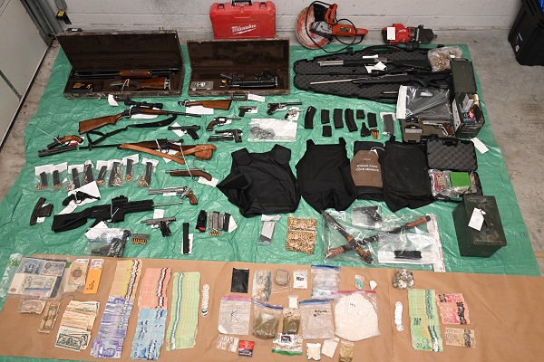 Seized items including firearms, ammunition, magazines, body armour, cash and other stolen property laid out on the floor.