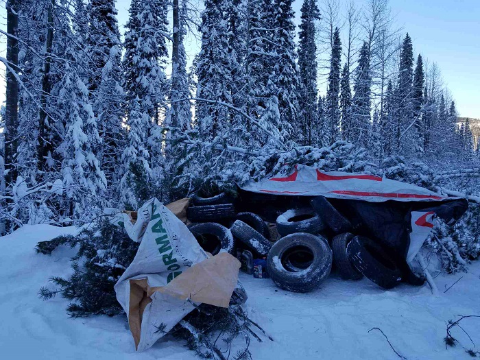 Photo of stack of tires with jugs of accelerants covered by tarps and trees