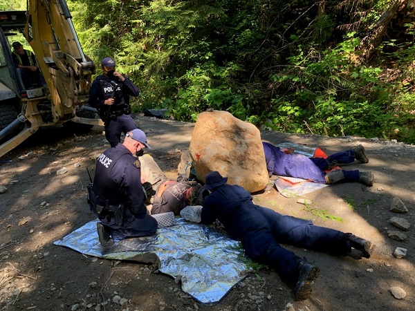 Photo of individual in a locking device on the ground next to a boulder