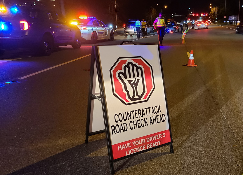 photo : panneau &laquo; Counter-Attack Road Check &raquo; sur la route, voitures de police aux gyrophares activ&eacute;s et c&ocirc;nes de signalisation en arri&egrave;re-plan
