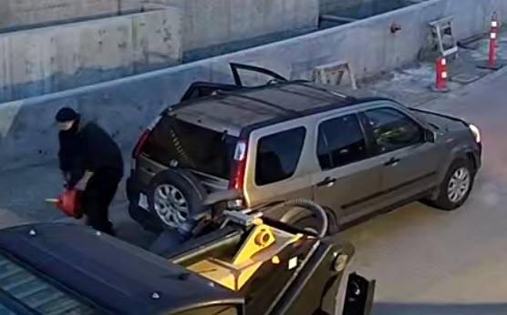 A heavier set, older person holds a red jerry can and stands in front of an older model brown or gold Honda CRV. 