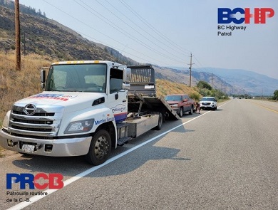 Vue lat&eacute;rale d&rsquo;une camionnette rouge qui s&rsquo;appr&ecirc;te &agrave; &ecirc;tre charg&eacute;e sur la plateforme d&rsquo;un camion de remorquage, sur l&rsquo;accotement de la route