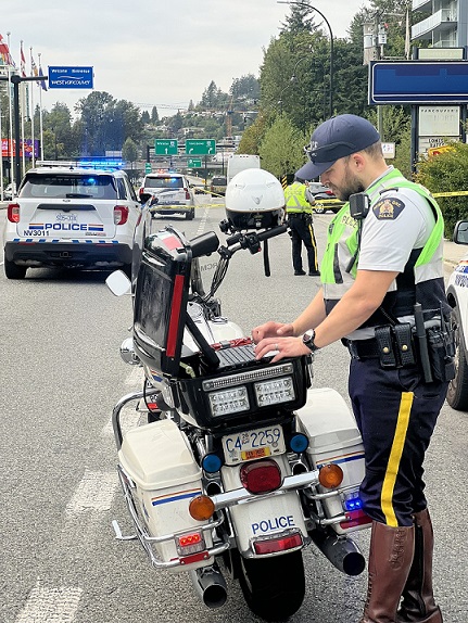 An RCMP officer working on his police laptop on the back of his motorcycle while investigating a collision.