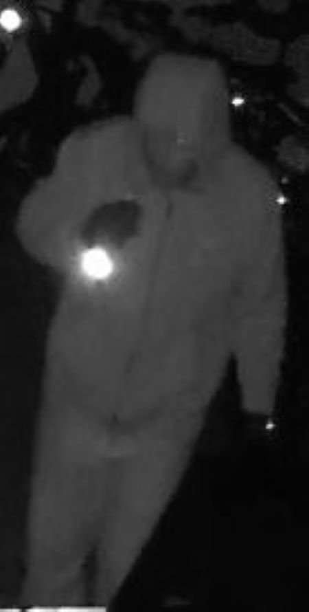 Suspect avec une lampe de poche : Un suspect v&ecirc;tu d&rsquo;une veste zipp&eacute;e et d&rsquo;un chandail &agrave; capuchon, montr&eacute; dans le mode de vision nocturne d&rsquo;une vid&eacute;o de s&eacute;curit&eacute;.