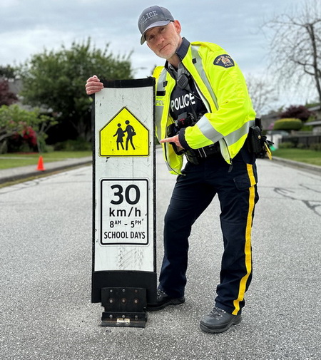 Photo of a police officer with the <q>30km/hr school days 8am &ndash; 5 pm</q> sign