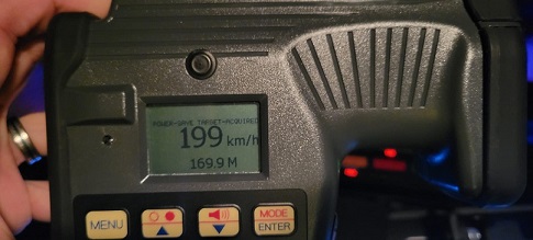 An officer holding a laser device with readings of 199 km/h 169.9 M