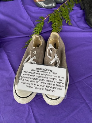 Pair of women&rsquo;s shoes placed on purple cloth with a biography placard that says, </q>Helene Colgan. Died: December 6, 1989. Helene (23) was in her final year of the mechanical engineering program and planned on getting her master&rsquo;s degree. She had three job offers waiting. Helene was one of 14 women killed at Ecole Polytechnique in Montreal.</q> 