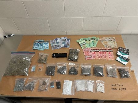 A variety of packaged drugs in white powder, pills, and leafy forms, as well as cash, cigarettes, and other items seized during an investigation.