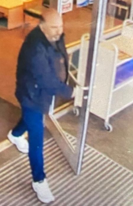 Un homme de forte carrure sort par la porte d&rsquo;un &eacute;tablissement. Il est v&ecirc;tu d&rsquo;un pantalon bleu et de chaussures de course blanches.