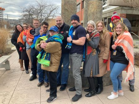 A group of people stand together in front of a monument, some with towels and toques.