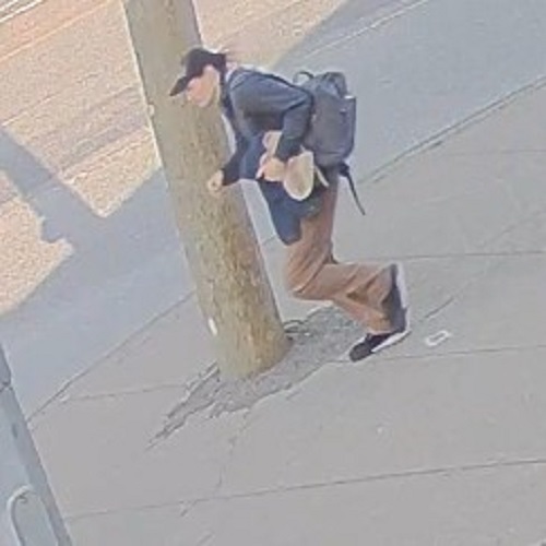 Left side profile of a man walking holding a dark blue coat