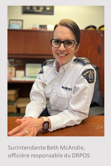 Photo d&rsquo;une femme blanche assise, les mains crois&eacute;es sur un bureau, et portant une chemise blanche &agrave; manche longue et des lunettes. Sous la photo, on peut lire : Surintendante Beth McAndie, offici&egrave;re responsable du d&eacute;tachement r&eacute;gional de Penticton-Okanagan-Sud-Silkameen.