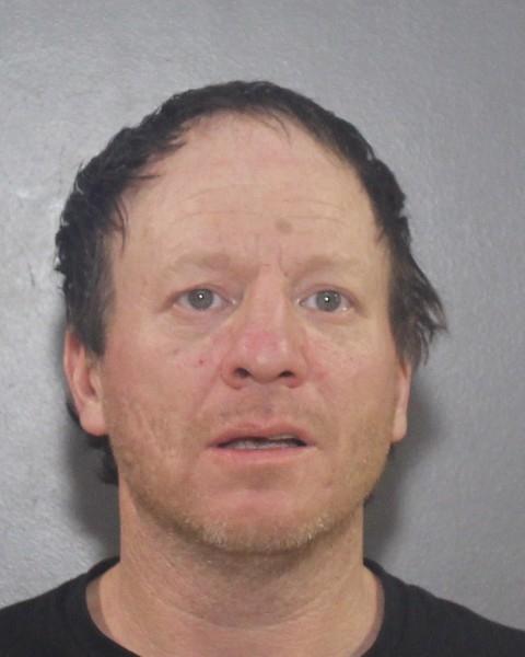 Homme de race blanche aux cheveux bruns clairsem&eacute;s v&ecirc;tu d&rsquo;un t-shirt fonc&eacute;, devant un fond gris.