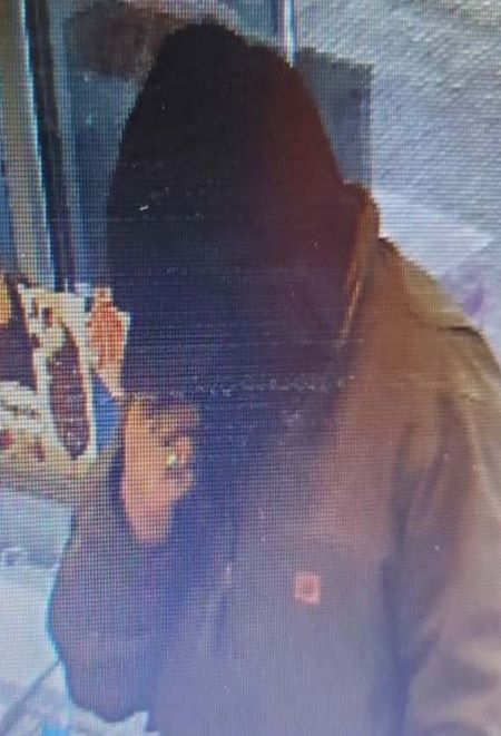 Un homme qui porte une veste beige avec une casquette et un capuchon. Seule sa main est visible.